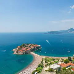 Idealne czarnogóra wakacje: wyspa Sveti Stefan z kamiennymi domkami i plażą pełną turystów, otoczona turkusowym morzem.