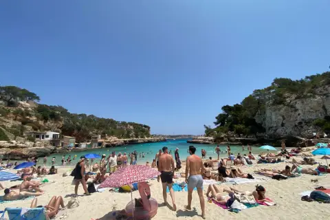 Słoneczna pogoda na Majorce, plaża pełna ludzi kąpiących się i opalających.