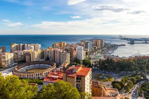Malaga, listopad: słoneczna pogoda nad miastem, morzem i portem. Widoczna arena, budynki mieszkalne i park.