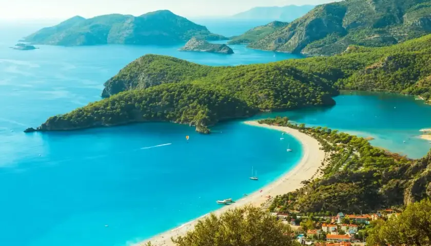 Turcja zachwyca turkusowym morzem i zielonymi wzgórzami. Widok na zatokę z plażą i łodziami.