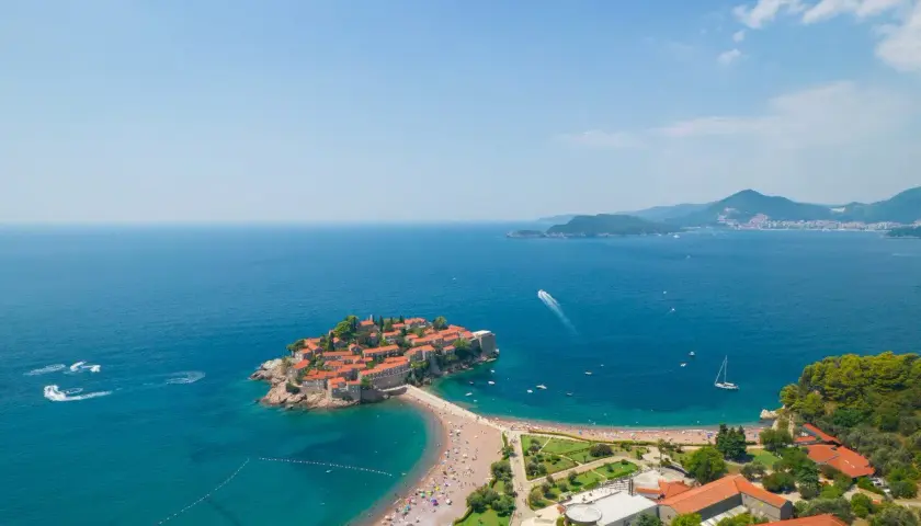 Sveti Stefan, Czarnogóra, z widokiem na turkusowe morze i zatłoczoną plażę.