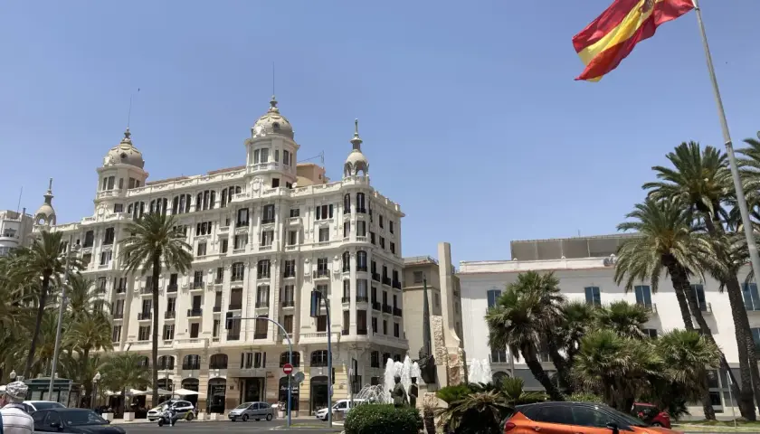 Alicante, pogoda marzec: słoneczny dzień, palmy i hiszpańska flaga nad białym budynkiem.