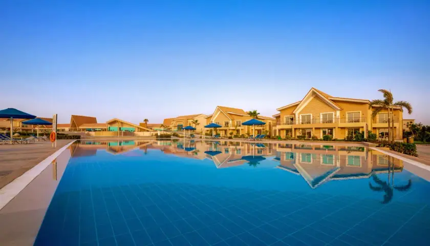 Basen hotelowy w Pickalbatros Sea World Marsa Alam z odbijającymi się w wodzie budynkami i palmami.