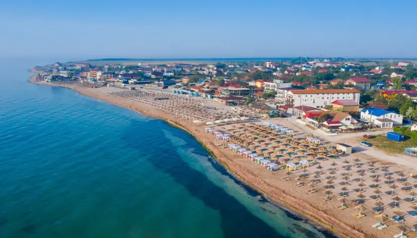 Plaża nad Morzem Czarnym z rzędami leżaków i parasoli. W tle zabudowania kurortu. Woda wygląda na ciepłą, idealną do kąpieli.