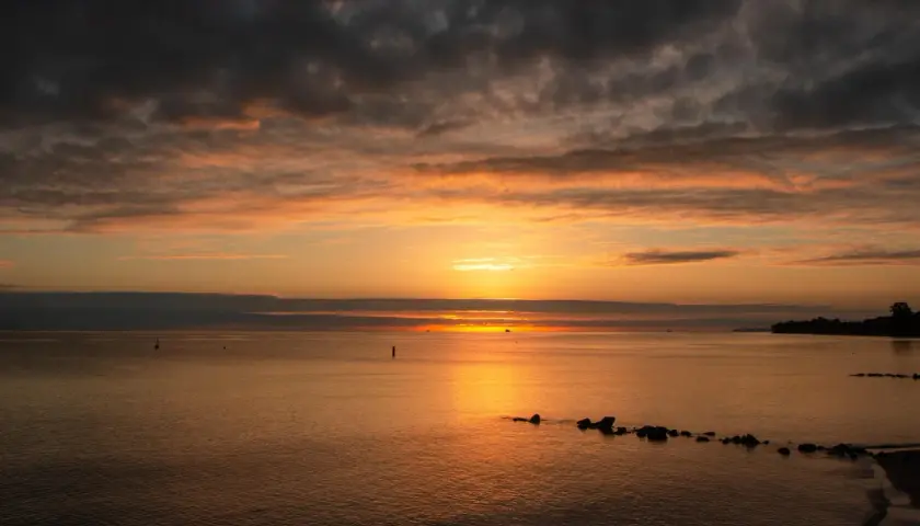 Zachód słońca nad spokojnym morzem. Czy nad oceanem jest jod? Woda lśni pomarańczem, chmury malują niebo.