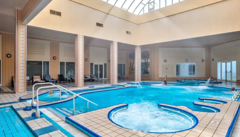 Wnętrze basenu z hydromasażem w Mahdia Palace. Woda jest turkusowa, a wokół basenu znajdują się leżaki.