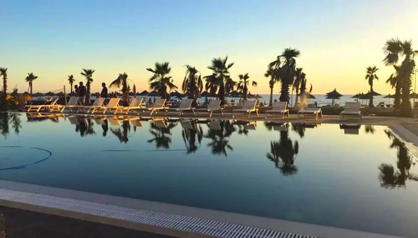 Zachód słońca nad basenem w Blumare Resort. Palmy i leżaki odbijają się w spokojnej wodzie.