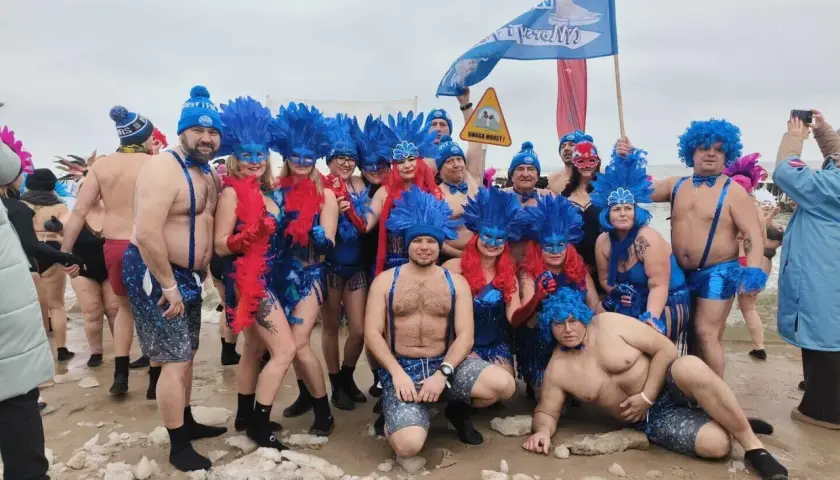 Grupa morsów w niebieskich piórach i maskach pozuje na plaży. Pewnie zastanawiają się, ile stopni ma Bałtyk w styczniu.