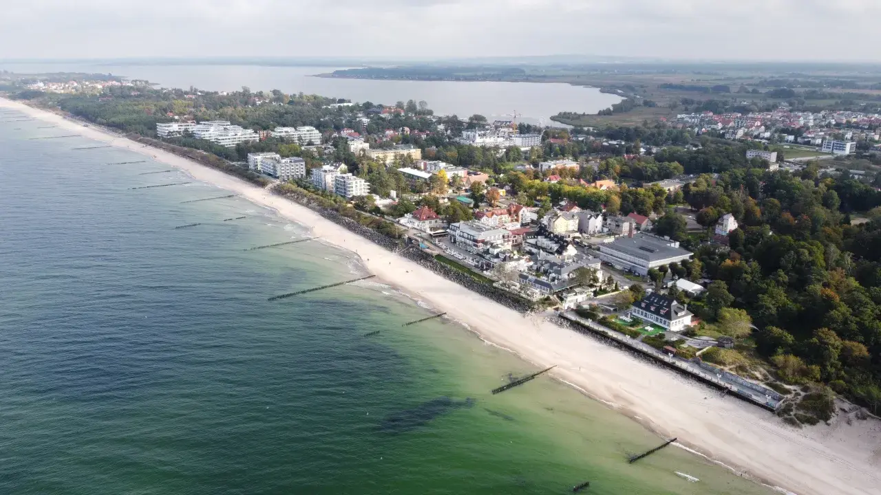 Widok z lotu ptaka na nadmorską miejscowość Mielno, z plażą, morzem i zabudowaniami. Ile mieszkańców ma Mielno? Tego nie widać, ale jest tu pięknie.