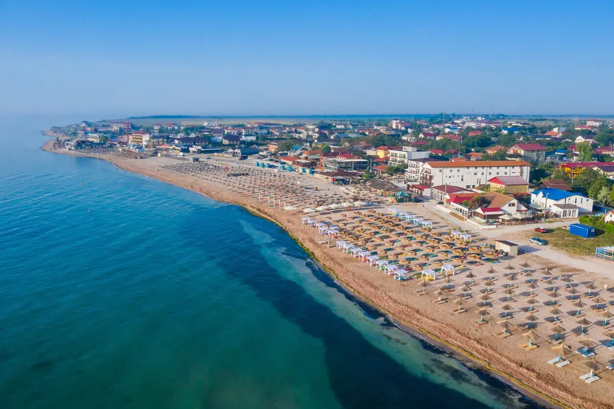 Plaża nad Morzem Czarnym z rzędami leżaków i parasoli. W tle zabudowania kurortu. Woda wygląda na ciepłą, idealną do kąpieli.