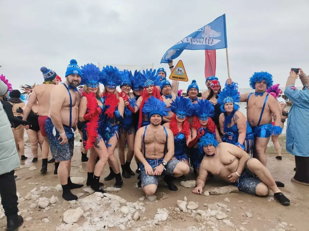 Grupa morsów w niebieskich piórach i maskach pozuje na plaży. Pewnie zastanawiają się, ile stopni ma Bałtyk w styczniu.