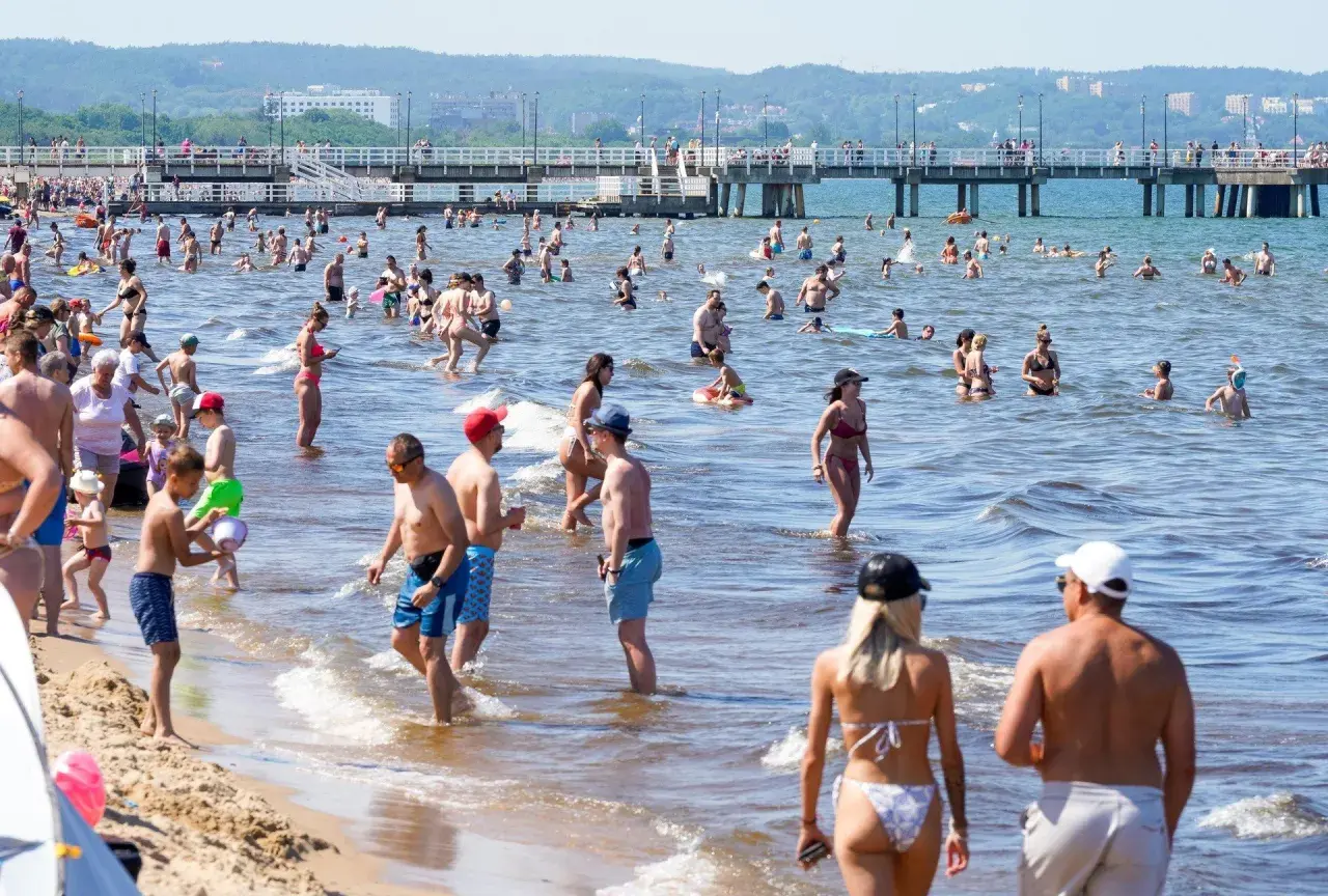 Tłum ludzi kąpiących się w morzu, wielu z nich w wodzie po pas. Czy Morze Czarne jest ciepłe? Tłumy plażowiczów sugerują, że tak!