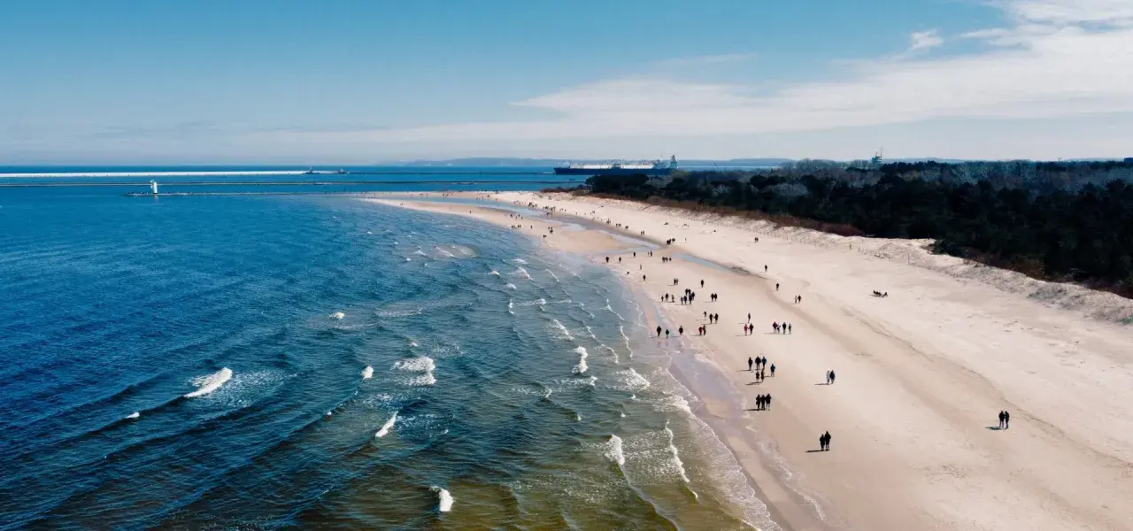 Spacer po plaży zimą to świetny pomysł na spędzenie czasu nad morzem. Widać ludzi spacerujących brzegiem morza.