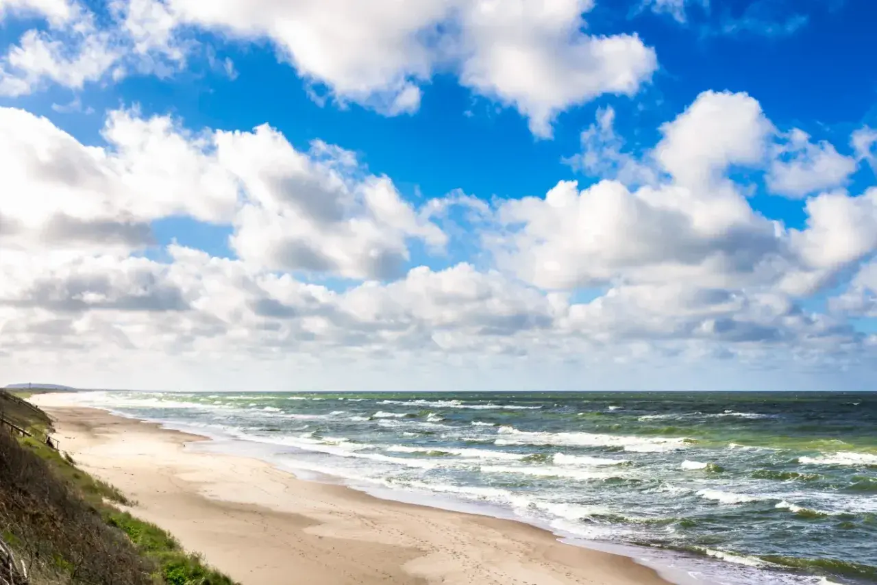 Plaża nad Bałtykiem, gdzie jest najcieplejsza woda? Piasek, fale i błękitne niebo z chmurami.