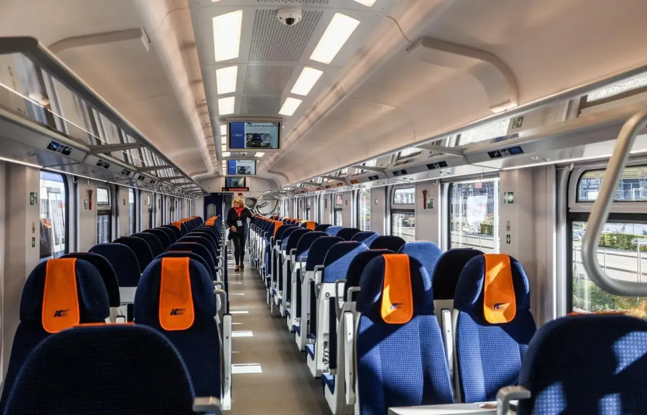 Wnętrze nowoczesnego pociągu PKP Intercity. Siedzenia w kolorze granatowym z pomarańczowymi zagłówkami. Pytanie: ile jedzie pociąg z Krakowa do Kołobrzegu?